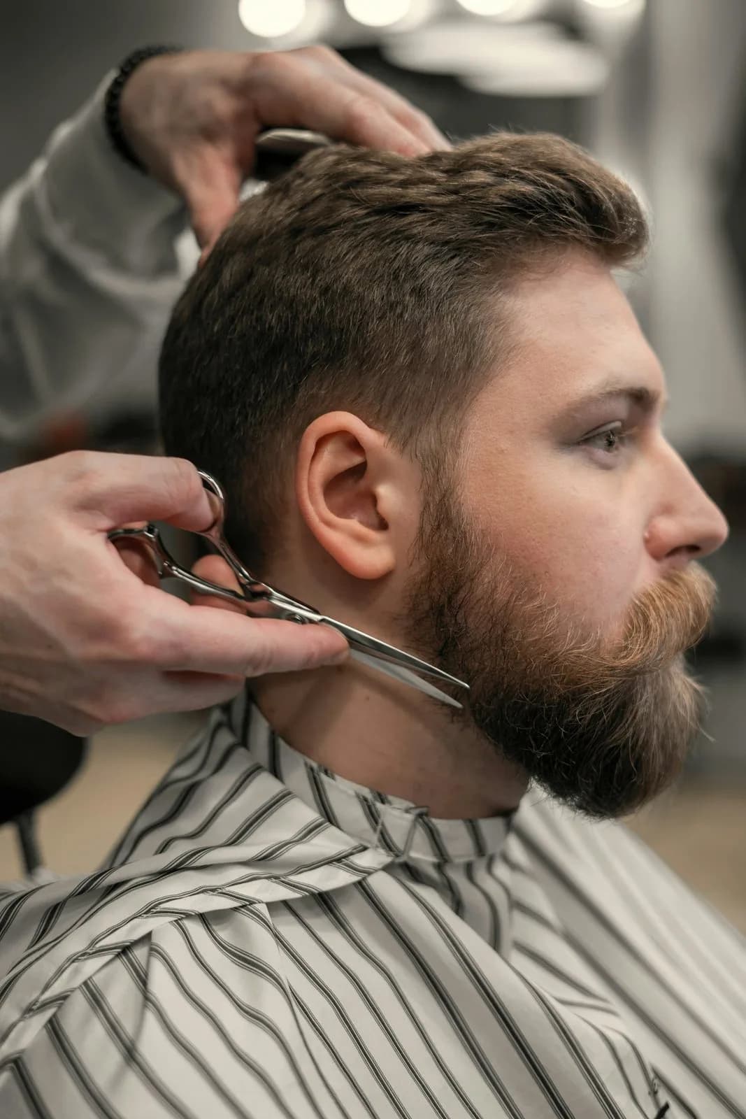 Taille de barbe aux ciseaux sur un client en cape rayée