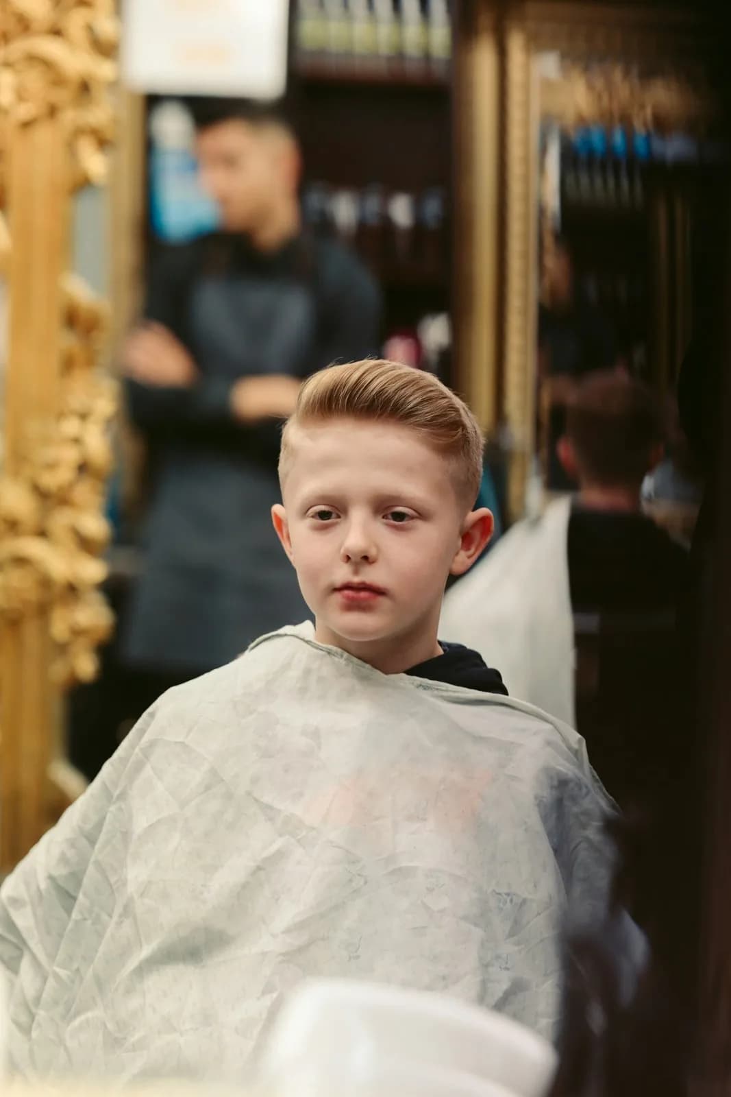 Petit garçon sous une cape de coupe dans un salon de coiffure
