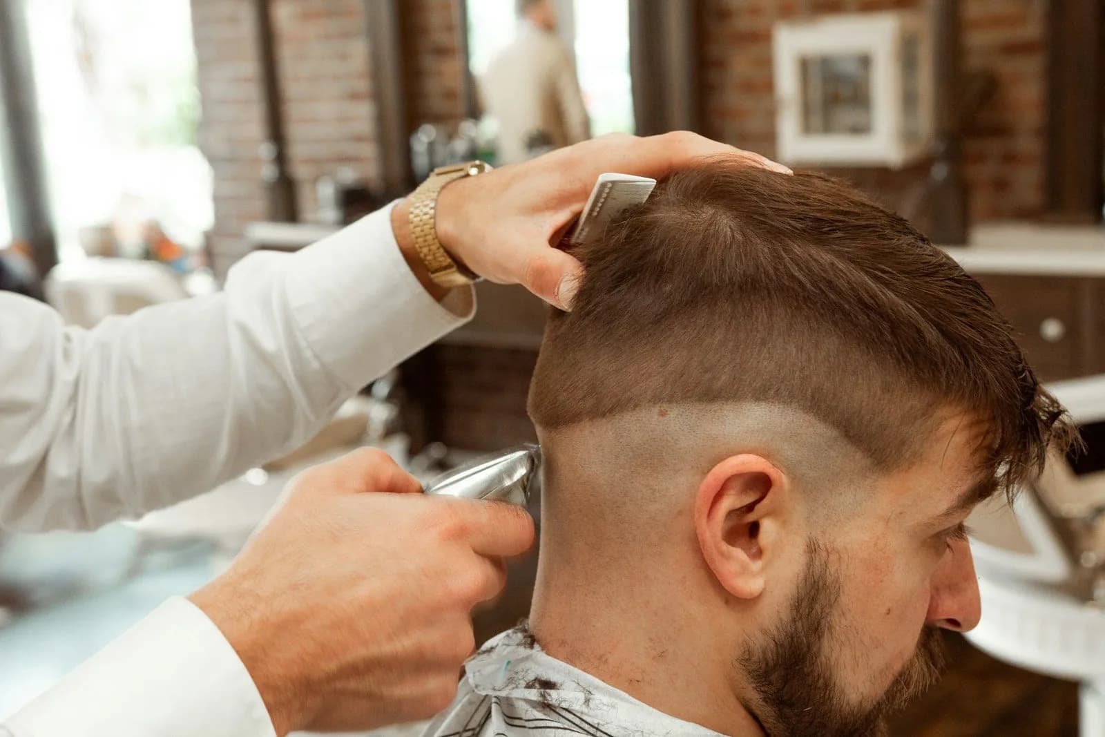 Coiffeur réalisant un dégradé à la tondeuse sur un client barbu
