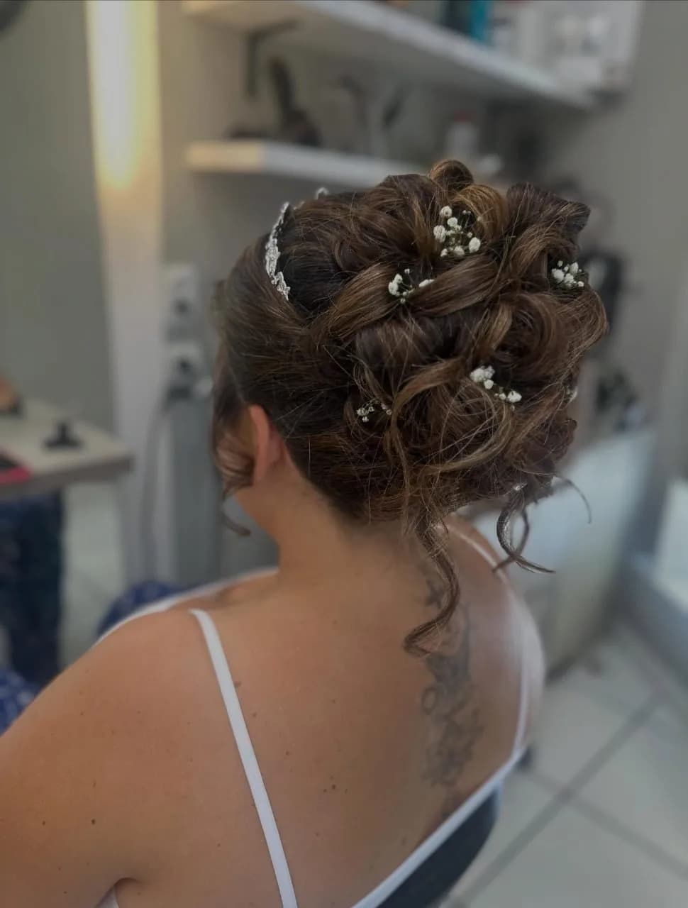 Chignon de mariage bouclé orné de petites fleurs blanches, vu de dos