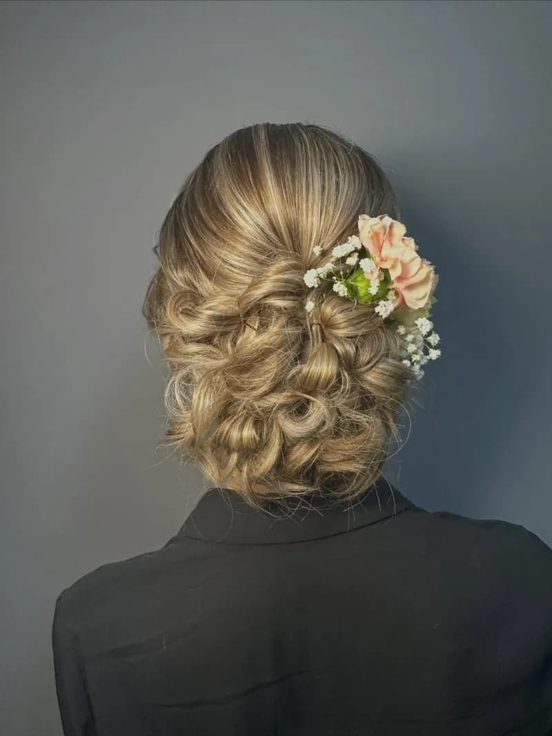 Chignon de mariage blond bouclé orné de fleurs roses, vu de dos