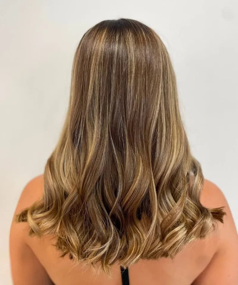 Cheveux mi-longs ondulés, mèches blond doré miel, vus de dos