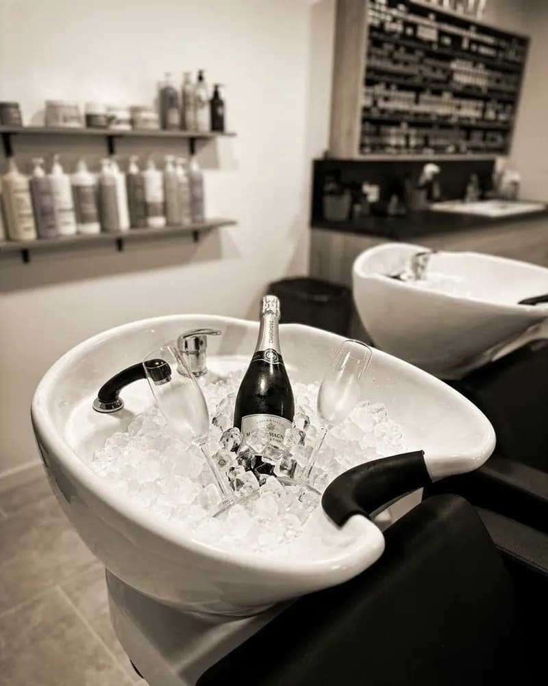 Un bac à shampoing du salon rempli de glace, avec une bouteille de champagne et des flûtes